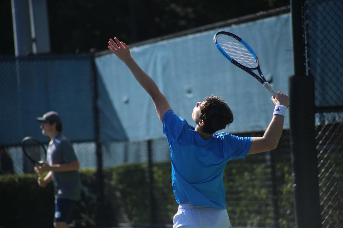 A player launches the tennis ball into the air as he prepares to serve to the opposing team. 