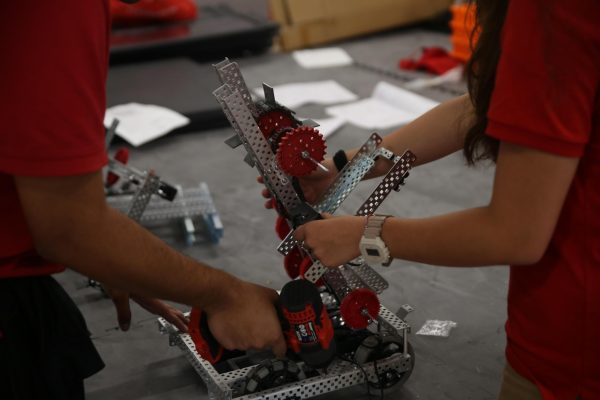 Robotics team students attach the secondary frame to the base motor and movement part of the robot. The metal frames are attached using screws and later electrical wiring is added to power the mechanics. 